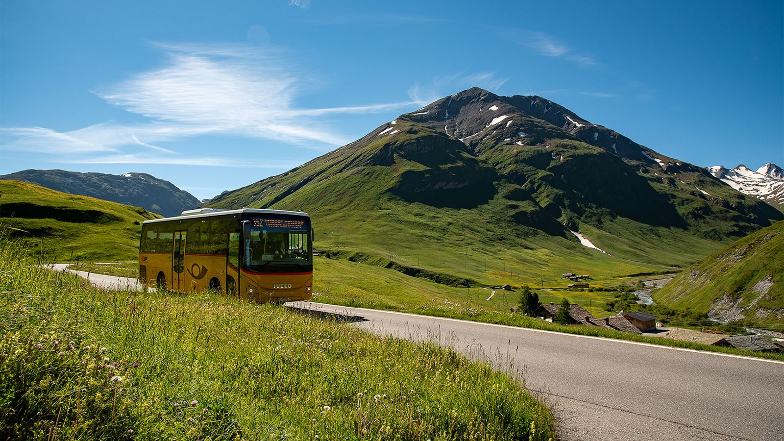 A Postbus travels through the mountainous landscape with green mountain meadows towards Juf.