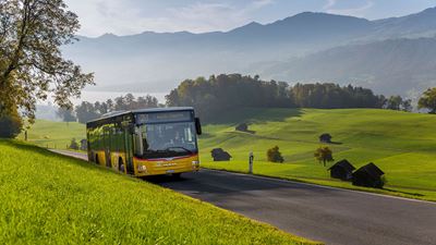 Landschaftsbild mit einem Postauto in Fahrt Richtung Flülie-Ranft. Im Hintergrund sieht man den Sarnersee sowie die Bergkette des Glaubenbielengebietes. © Mike Niederhauser Merlin Photography