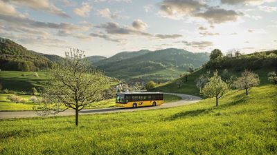 Postauto in einer Kurve inmitten grüner hügeliger Landschaft.