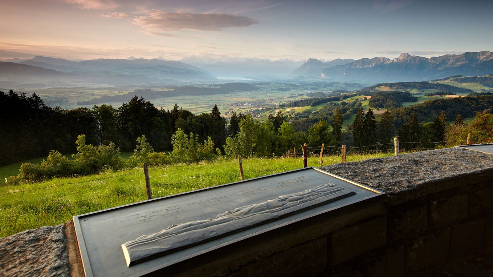In the foreground, a board with information about the mountain range in the background. View of the Gantrisch mountain range and Lake Thun.
