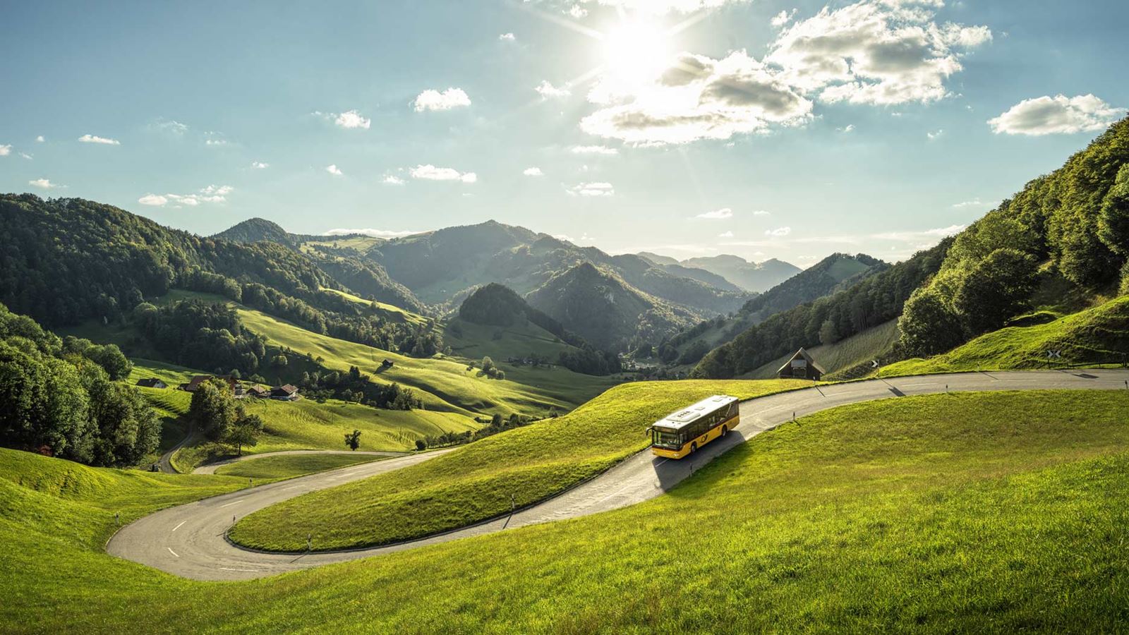 Das Postauto fährt den Passwang herab. Die grüne, hügelige Landschaft ist im Hintergrund zu erkennen.