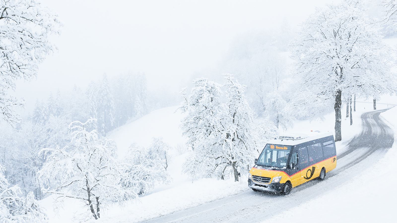 Ein kleines Postauto fährt durch die verschneiten Strassen von Sternenberg