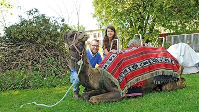 Ragazza e uomo con un cammello seduto su un prato nella fattoria di Ben a Oberglatt