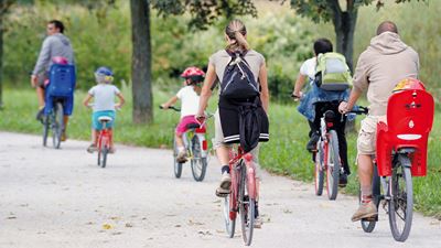 Adults and children cycle past green trees around Zurich Airport.