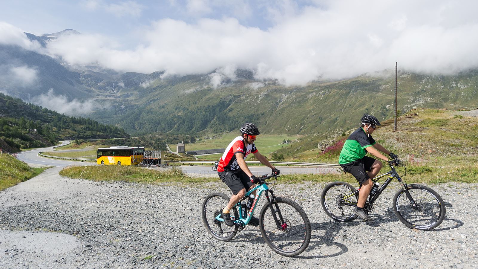Deux vététistes sur le col du Simplon. On aperçoit un car postal à l’arrière-plan.