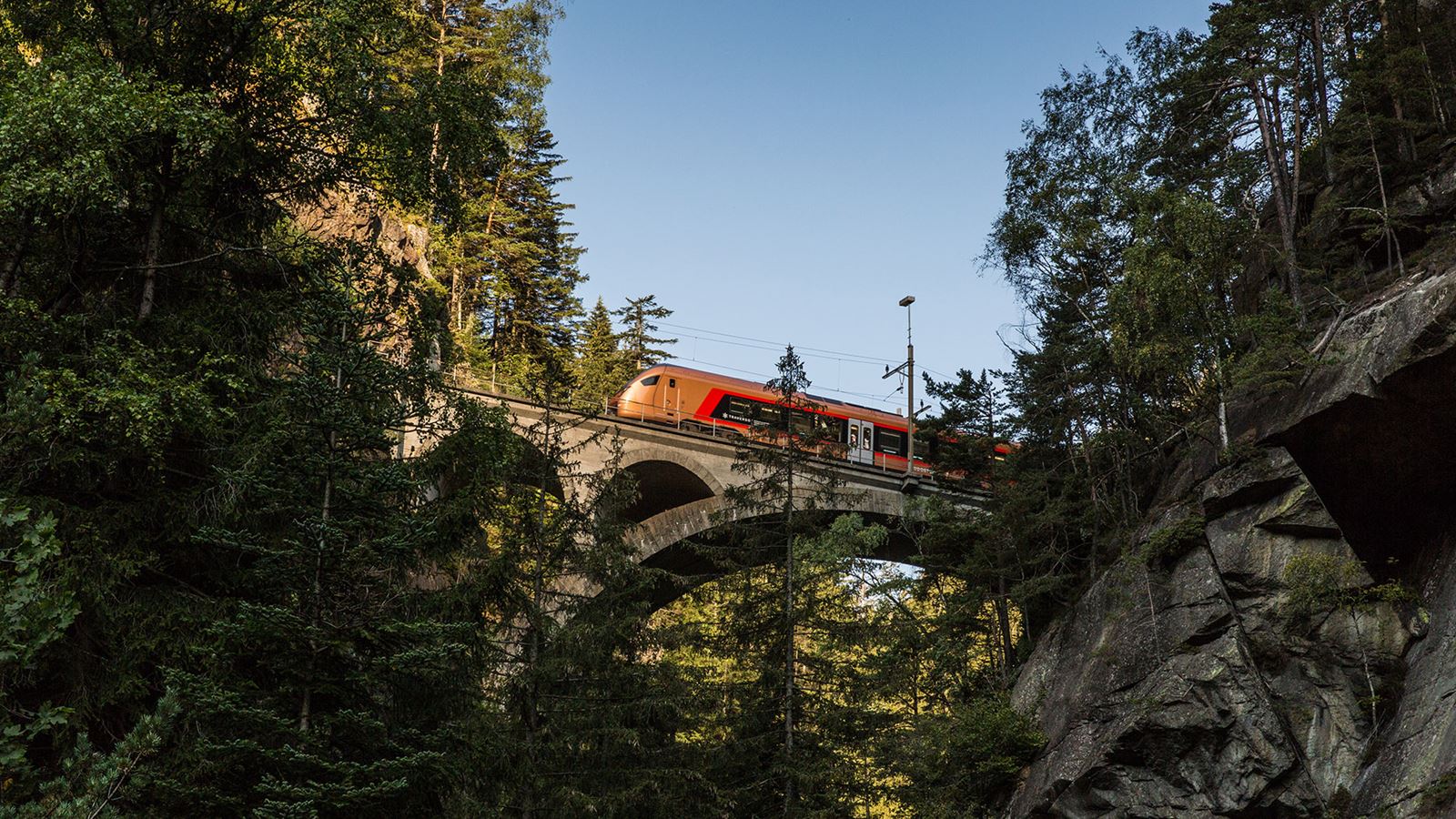 SOB-Zug auf einer Steinbrücke inmitten eines bewaldeten Tals bei klarem Himmel.