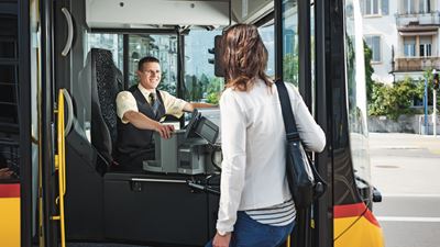 A woman boards a Postbus on the driver’s side. The driver smiles at her as he greets her.