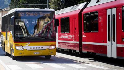 Postauto neben einem Zug der Rhätischen Bahn.