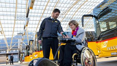 Un conducteur CarPostal montre quelque chose sur son téléphone mobile à une femme en fauteuil roulant