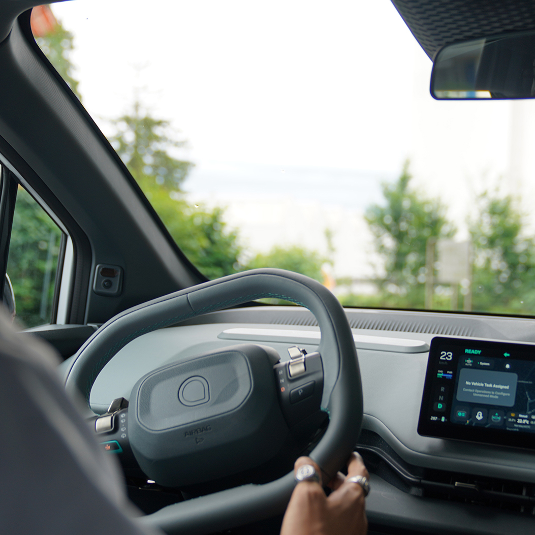Person sitzt am Steuer eines modernen Autos; auf dem Display ist ein Navigationssystem zu sehen
