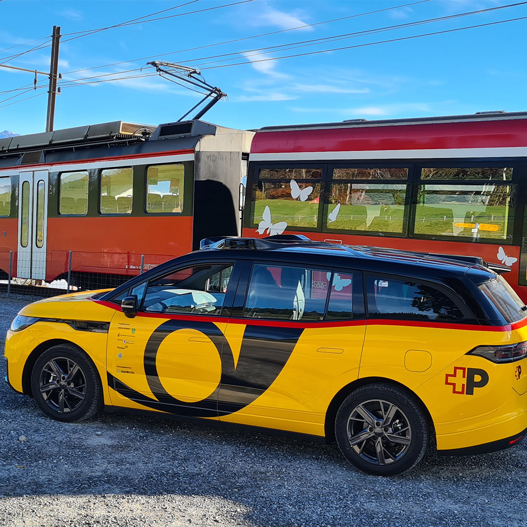 Le véhicule AmiGo se trouve à côté d’un train sur une ligne ferroviaire en zone rurale.