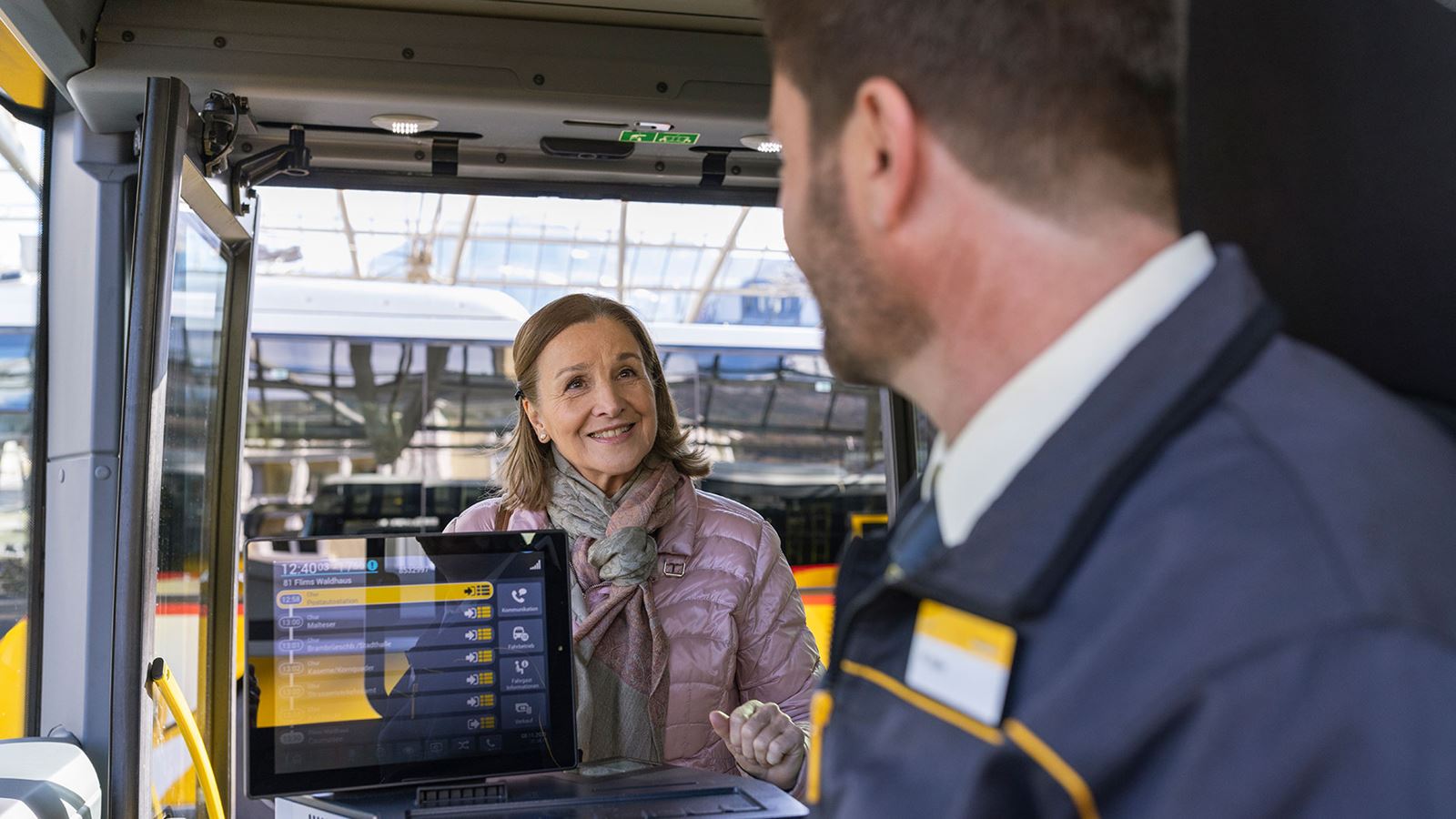 Frau steigt in Postauto ein und wird von Fahrer freundlich begrüsst.    