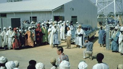 Der Emir von Kano mit seinem Cadillac umgeben von vielen Menschen mit Kopftüchern und langen Kleidern.