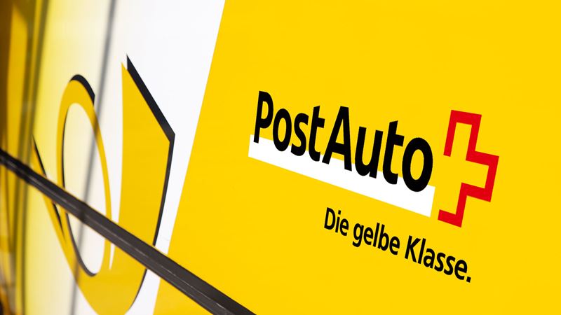 Eine Nahaufnahme eines Postauto auf welches man den Firmennamen, das Posthorn und den Claim “Die gelbe Klasse” sieht.