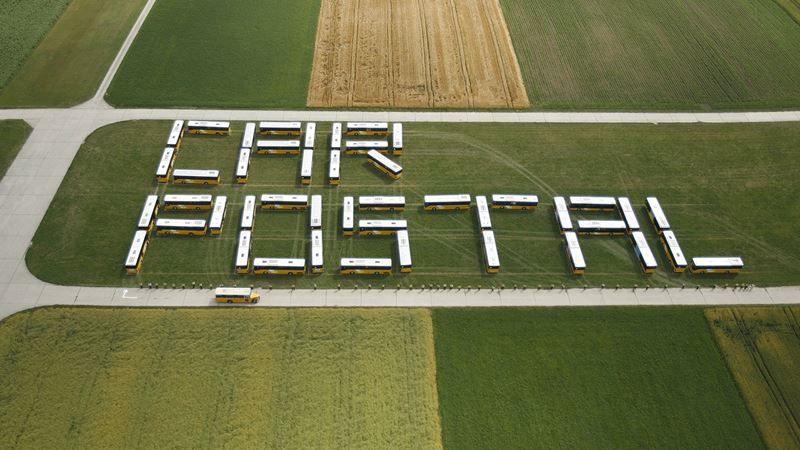 The aerial photo shows several Postbuses that have been arranged to form the words “Car Postal”.