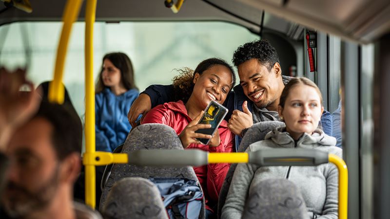A smiling couple sitting in a Postbus and taking a selfie.