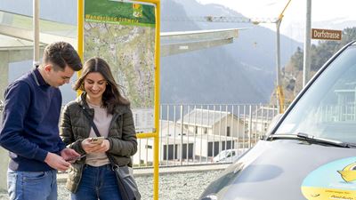 Zwei Jugendliche stehen vor einem PubliCar und schauen auf ihr Smartphone.