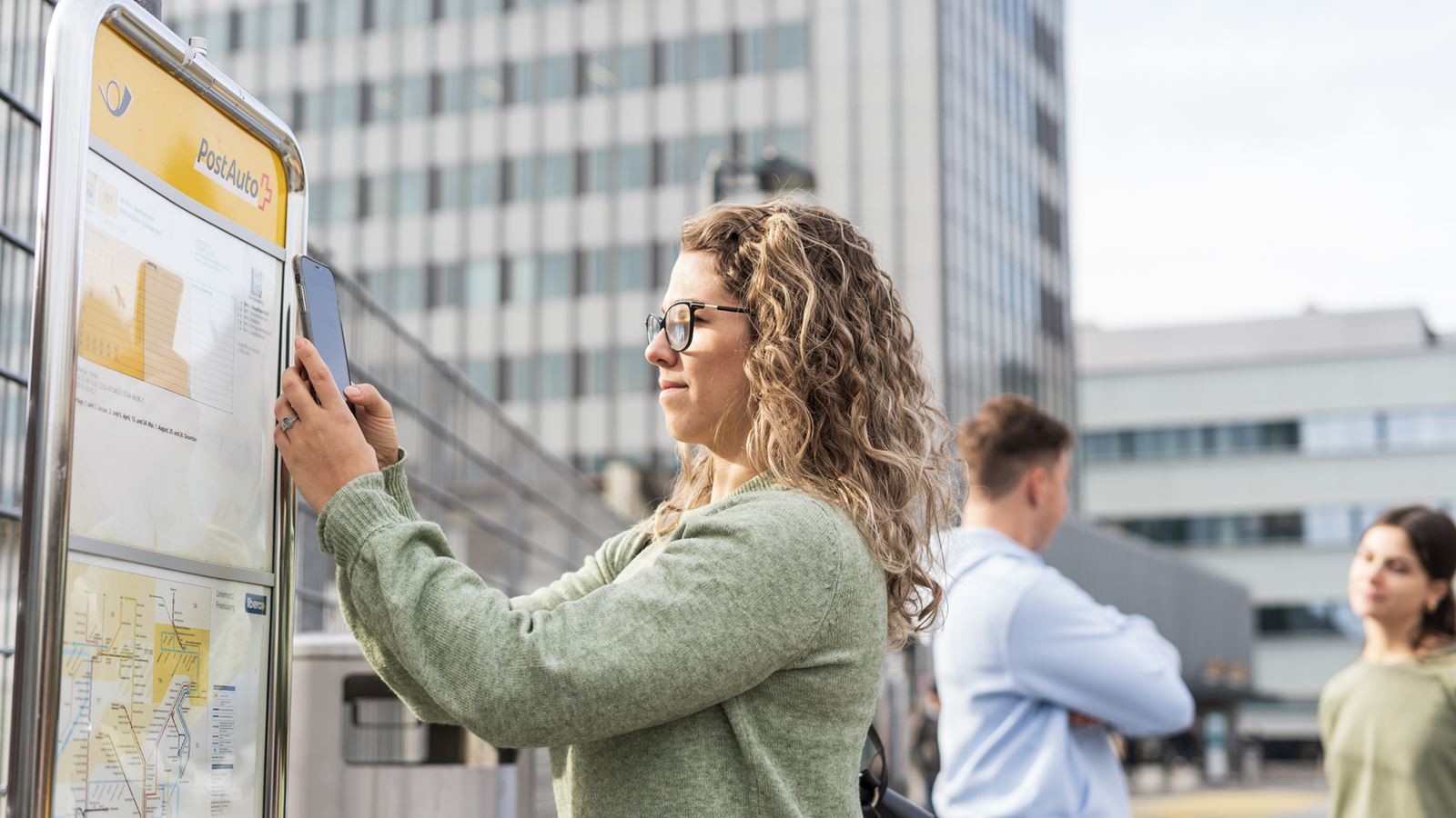 Une femme scanne le code QR de l’horaire à l’arrêt de car postal de Berne avec son téléphone mobile.