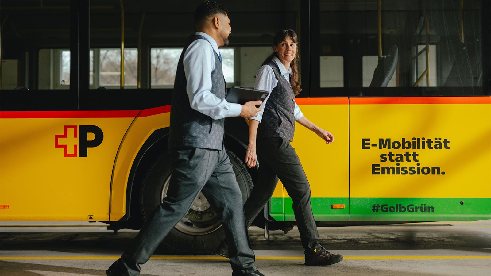 Eine Fahrerin und ein Fahrer neben einem Postauto