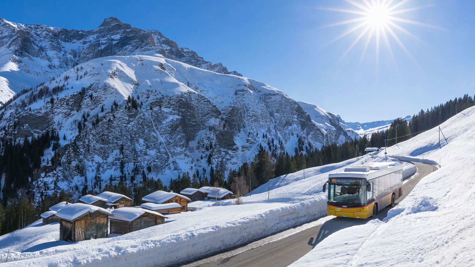 Ein Postauto fährt durch ein verschneites Bündner-Tal bei schönem Winterwetter.